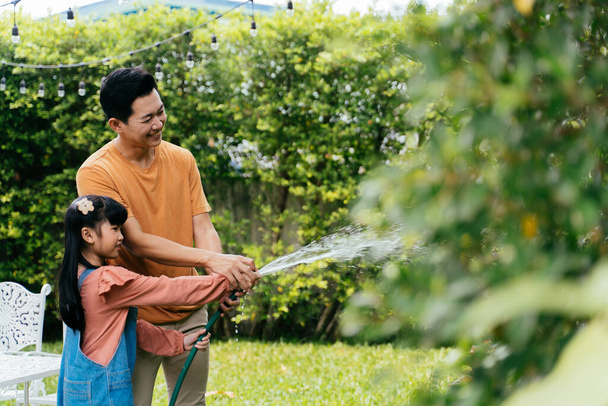 Happy Asian family of father and daughter watering the plants abd bush at home. Spending time together in garden - Foto, immagini