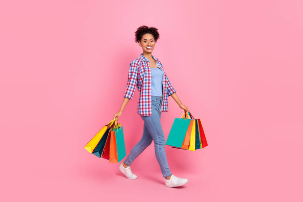Full length body size view of attractive cheerful girl going holding bags clothes isolated over pink pastel color background - 写真・画像