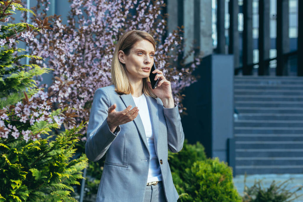 Serious business woman talking on the phone outside the office - 写真・画像