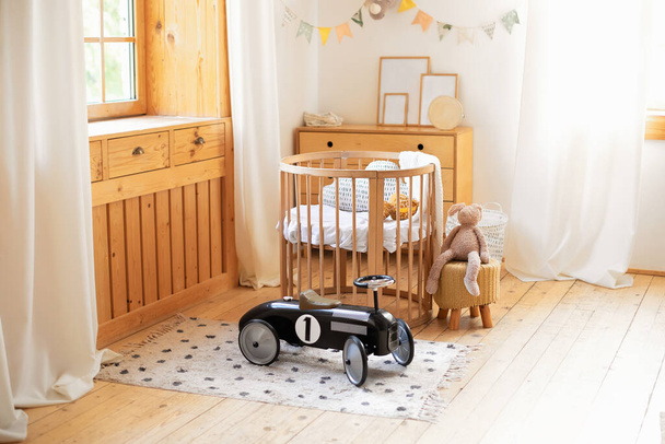 Retro style child toy racing car in children room. Modern interior of a children's bedroom. Copy space. Hygge. Kindergarten. Cozy Scandinavian lights baby room: wooden crib with bedding and plush toy - Photo, Image