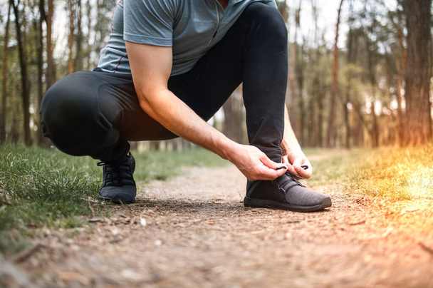 Man tying sneakers. Male runner jogging at the park. Guy training outdoors. Exercising on forest path. Healthy, fitness, wellness lifestyle. - Photo, image