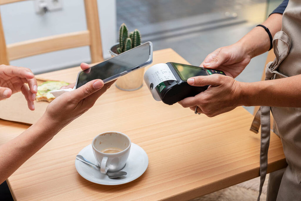 paying with a mobile app through a payment terminal in the hands of the waitress in a bar or cafeteria - Photo, image