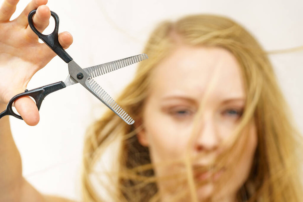 Young woman holding special chunking shears, tool for work of hairdresser. Coiffure hairstyle and haircut. - Foto, imagen