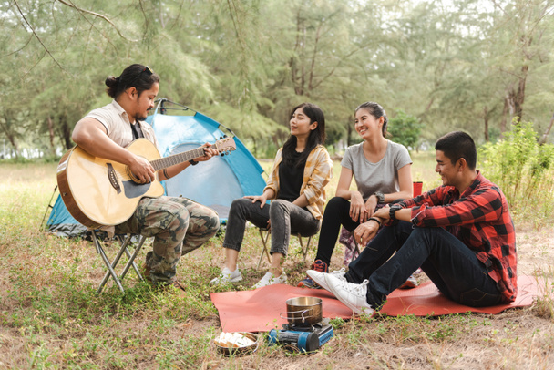 W lesie, Azjaci męscy i żeńscy podróżnicy biwakują i imprezują, rozmawiają, śpiewają i grają na gitarze.. - Zdjęcie, obraz