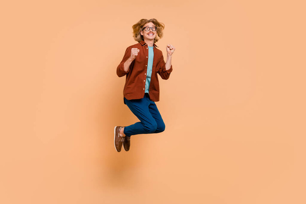 Full length body size view of attractive cheerful lucky guy jumping rejoicing having fun isolated over beige pastel color background - Foto, afbeelding