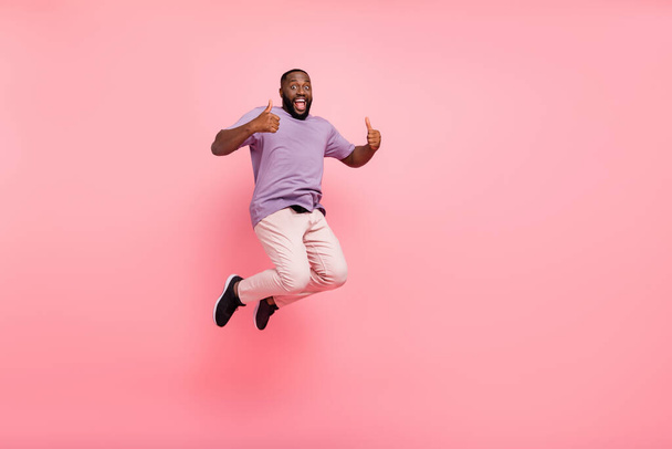 Photo of excited pretty guy wear purple t-shirt jumping high thumbs up empty space isolated pink color background - Foto, Bild
