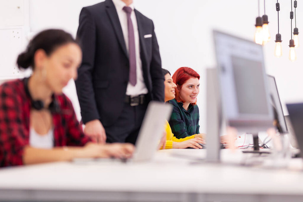 Gruppe multiethnischer Kollegen, die in einem modernen Büroraum an Desktop-Computern arbeiten. Mädchen ruht mit Füßen auf Tisch - Foto, Bild