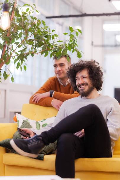 Happy colleagues sitting on a sofa in modern coworking office space. - Fotó, kép