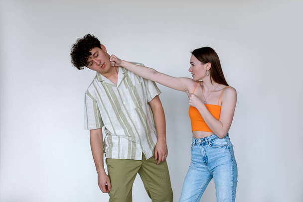 Portrait of young couple posing on white background. Young displeased woman punching fainting man with closed eyes. - Fotoğraf, Görsel