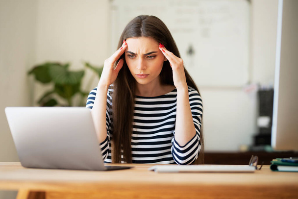 Female entrepreneur with headache sitting at desk. Businesswoman under terrible physical tension at work. Home office. - Φωτογραφία, εικόνα