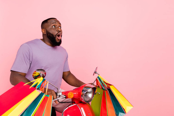 Photo of excited shocked guy dressed violet t-shirt driving moped holding bags empty space isolated pink color background - Foto, imagen