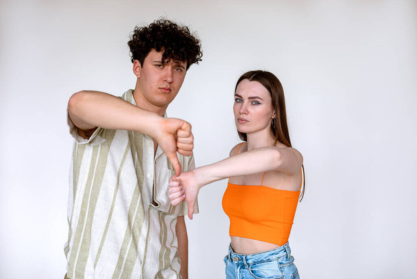 Portrait of young displeased couple posing on white background. Young upset unhappy man, woman showing thumbs down sign. - Фото, изображение