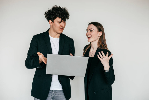 Portrait of young overemotive couple wearing black. Young pleased man holding ans showing laptop to overjoyed woman. - Fotó, kép