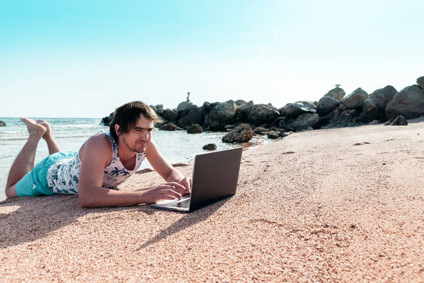 een man met een laptop op een zand rust en werkt als freelancer - Foto, afbeelding