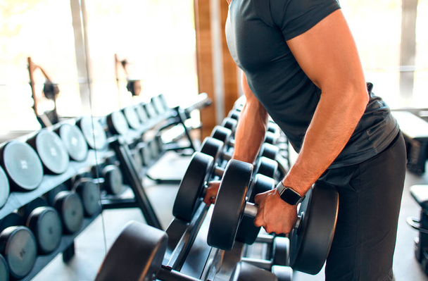 Izmos sportos férfi a sportruházatban, aki súlyzókkal gyakorol bicepszre egy edzőteremben. A sport és a szabadidő fogalma. - Fotó, kép