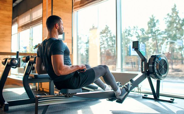 Muscular young man in sportswear doing exercises on the simulator in the gym club. The concept of sports and recreation. - Photo, image