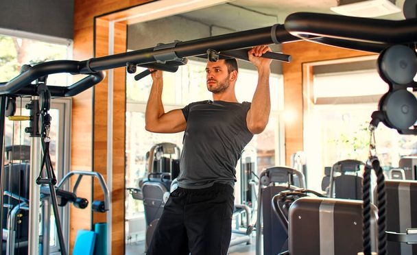 Caucasian muscular man in sportswear pulls up on the horizontal bar in the gym. The concept of sports and recreation. - Φωτογραφία, εικόνα