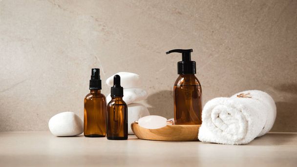 Set of glass bottles with face cosmetics and a white towel on a light background with white stones. Banner - Photo, image