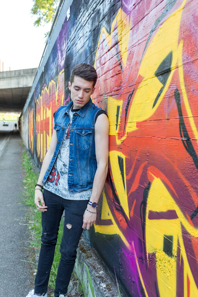 beautiful dark brown street style guy with jeans jacket in a street with graffiti. High quality photo - 写真・画像