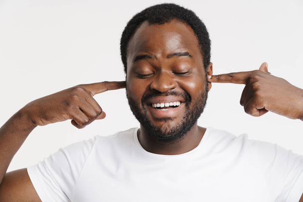 Black bristle man dressed in t-shirt smiling while plugging his ears isolated over white background - Photo, Image