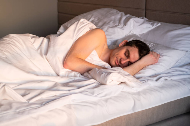 Jóképű férfi alszik az ágyában a napsütéses reggelen. - Fotó, kép