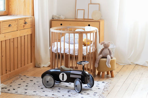 Retro style child Black racing car in a children room. Modern interior of child bedroom. Hygge. Kindergarten. Cozy Scandinavian baby room: crib with bedding and toys. Light Room with Wooden Cot Cradle - Фото, изображение