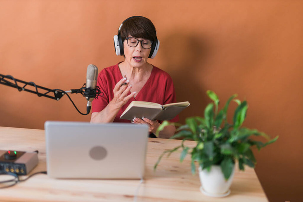 Μεσήλικες παρουσιάστρια ραδιοφώνου μιλώντας στο μικρόφωνο και διαβάζοντας ειδήσεις - ραδιοφωνική μετάδοση online concept - Φωτογραφία, εικόνα