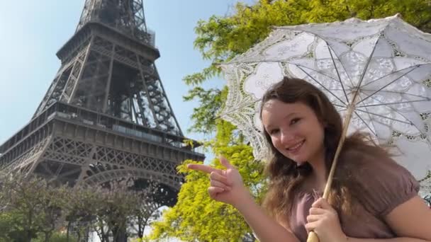 a beautiful teenage girl looks into the frame leaning against the backdrop of the Eiffel Tower She smiles and seems to be showing come here great advertisement for a trip to Paris - Footage, Video