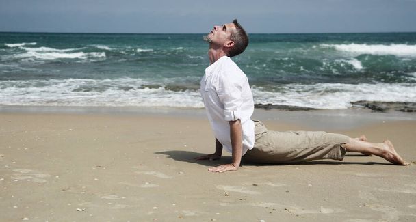 Yoga lesson. A man practices yoga near the sea. - Foto, afbeelding