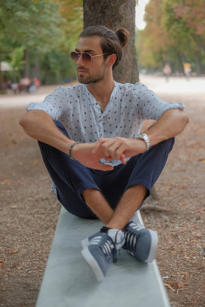 bel ragazzo italiano dai capelli scuri con camicia seduta sulla panchina del parco Ducale di Parma. Foto di alta qualità - Foto, immagini