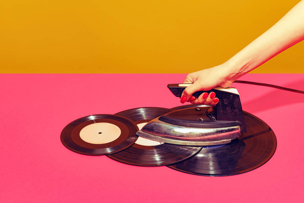 Colorful bright image of woman using retro iron and ironing vintage vinyl records isolated over pink background. Creativity - Foto, Imagen