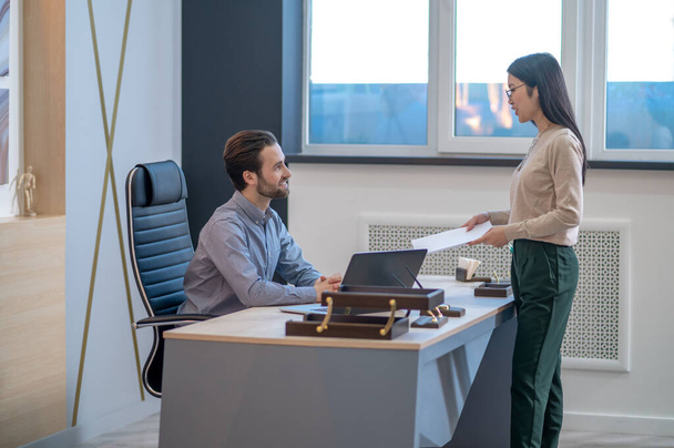 Assistant handing papers to her boss in his office - Foto, Imagen