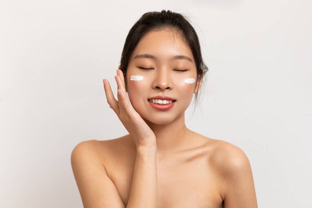 Bellezza ritratto di donna asiatica toccare applicando crema sulla guancia - Foto, immagini