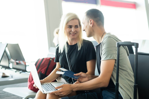 couple assis avec ordinateur portable, téléphone et valise dans la salle d'attente de l'aéroport. Concept de voyage d'affaires - Photo, image