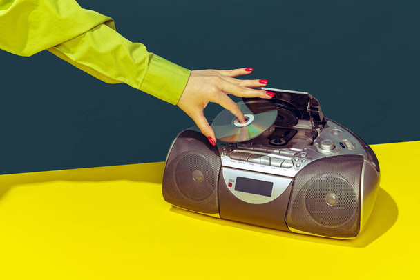 Colorful image of vintage radio player on bright yellow tablecloth isolated over dark green background. Putting music disk - Foto, afbeelding