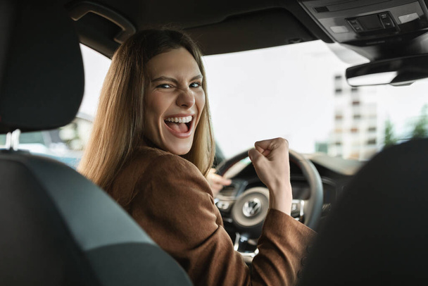 Mujer joven emocionada celebrando la compra exitosa de coches, haciendo un gesto SÍ mientras se sienta dentro del salón de automóviles en la concesionaria - Foto, imagen