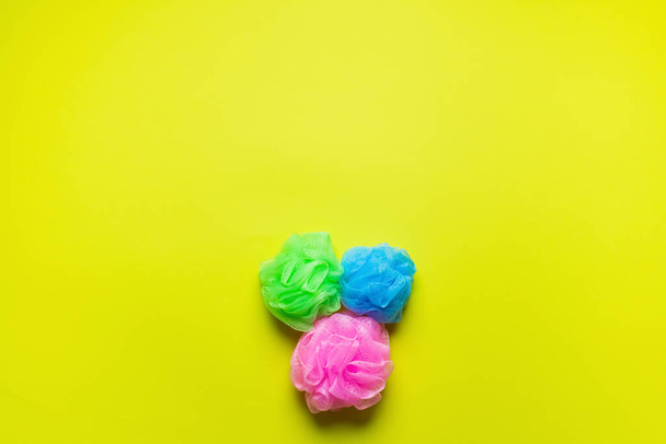 top view of pink, blue and green body puffs on yellow background with copy space - Φωτογραφία, εικόνα