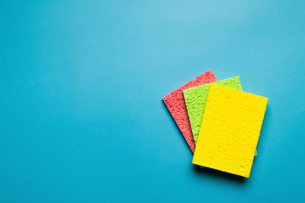 top view of bright yellow, green and pink sponge cloths on blue background - Foto, afbeelding