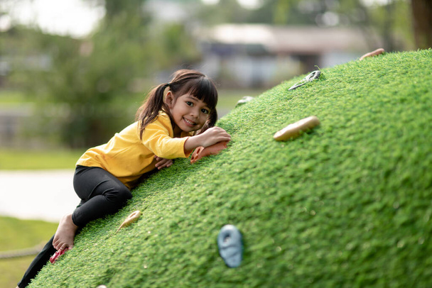 Linda chica asiática que se divierte tratando de escalar rocas artificiales en el patio de la escuela, Niña trepando por la pared de roca, Coordinación Mano y Ojo, Desarrollo de habilidades - Foto, Imagen