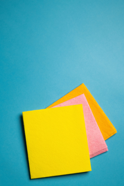 top view of bright yellow, pink and orange dishrags on blue background - Fotó, kép