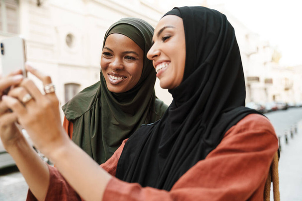 Multiracial muslim women using mobile phone during walking on city street - Фото, зображення