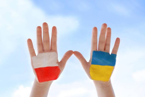 Flags of Poland and Ukraine. Two painted children's palms against blue sky. Unity solidarity help concept - Foto, afbeelding