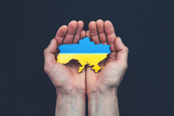 Male hands hold map of Ukraine on black background. Save or help concept - Foto, Bild