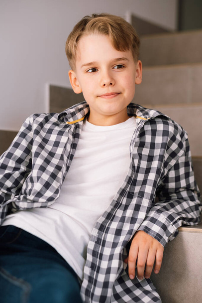 Elegante chico adolescente sonriendo mientras posando para una hermosa foto mientras está sentado en los escalones. - Foto, Imagen