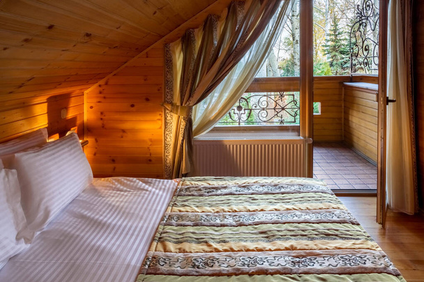 Затишна спальня з обробкою з натурального дерева з двоспальним ліжком і балконом
 - Фото, зображення