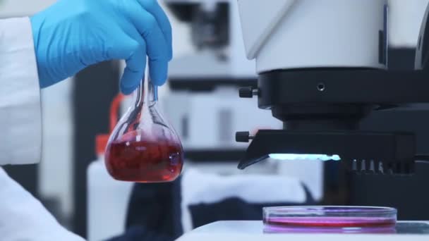 Naukowiec mieszający różowy płyn w szklanych kolbach - Materiał filmowy, wideo