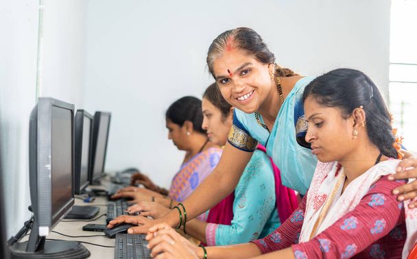 村の女性にコンピュータ教室を教えている間にカメラを見て笑顔の先生-ボランティアの概念、自己雇用訓練とエンパワメントプログラム - 写真・画像