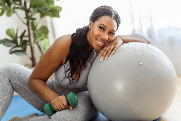 An African american woman working out in home livingroom gym with training ball - Фото, изображение