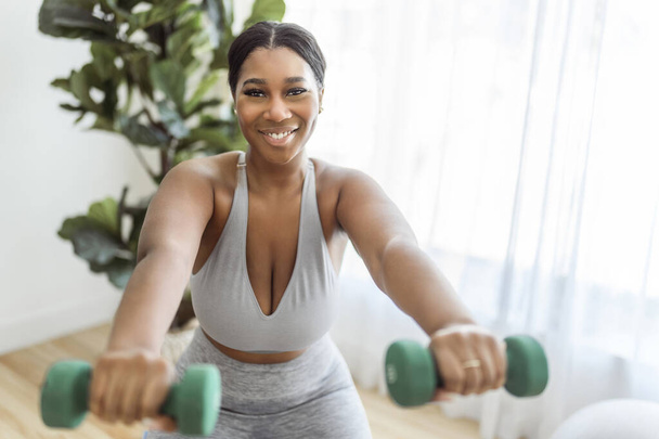 An African american woman working out in home livingroom gym lift dumbbell - Fotografie, Obrázek