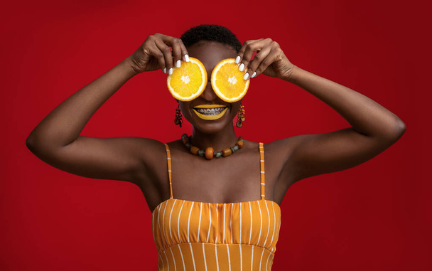 Joyful black lady holding orange circles over her eyes - Foto, Imagem